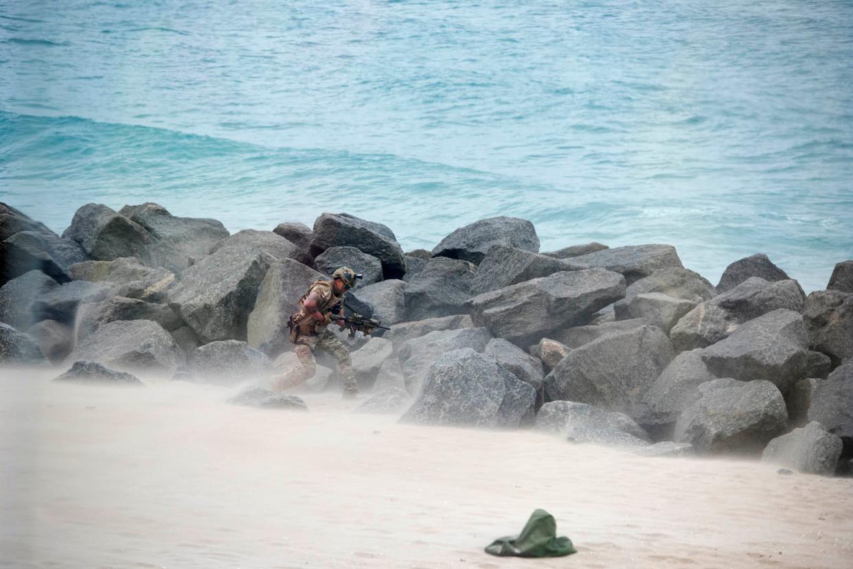 A Navy SEAL waits on the beach after repelling from a helicopter.