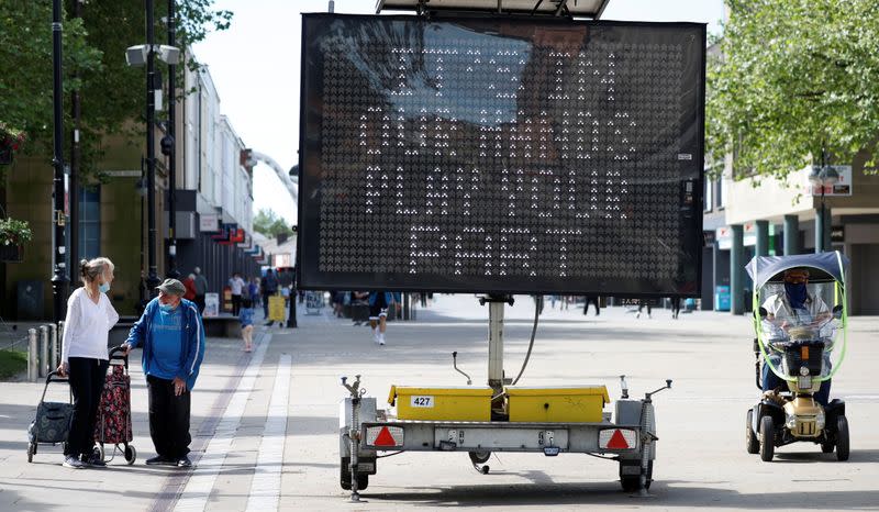 People walk past an information board, amid the COVID-19 outbreak, in Bolton