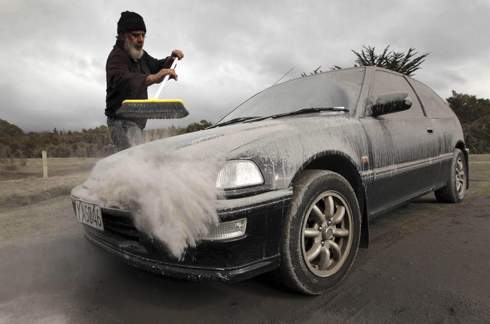 Vic Cassin sweeps ash from a car in Rangipo near Mount Tongariro, New Zealand after an eruption, Tuesday, Aug. 7, 2012. The volcano in New Zealand's central North Island has erupted for the first time in more than a century, sending out an ash cloud that is causing road closures and the cancellation of some domestic flights. (AP Photo/New Zealand Herald, Alan Gibson) AUSTRALIA OUT, NEW ZEALAND OUT