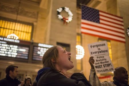 An American flag is seen in the background as an activist, demanding justice for the death of Eric Garner, holds her hands to her throat while shouting,"I can't breath," during a protest with dozens of others at Grand Central Terminal in the Manhattan borough of New York December 11, 2014. REUTERS/Adrees Latif