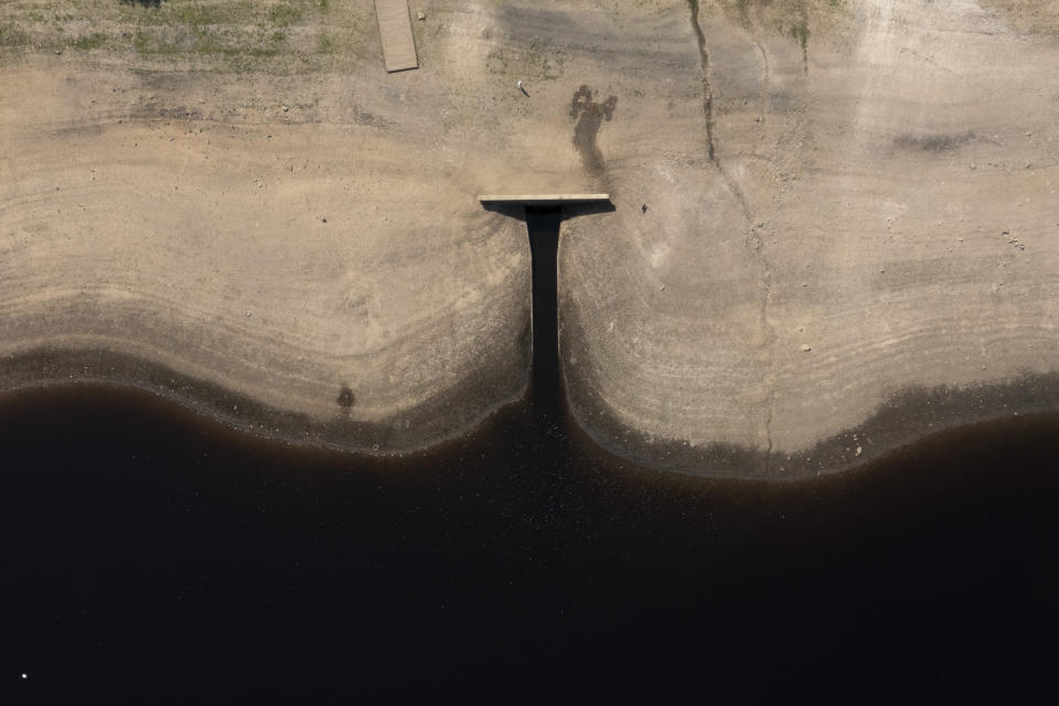 A member of the public walks a dog at Scammonden Reservoir in West Yorkshire, England, Monday, July 18, 2022 as reservoir levels dip dangerously low amid record high temperatures in the UK. Millions of people in Britain stayed home or sought shade Monday during the country's first-ever extreme heat warning, as hot, dry weather that has scorched mainland Europe for the past week moved north, disrupting travel, health care and schools. (AP Photo/Jon Super)