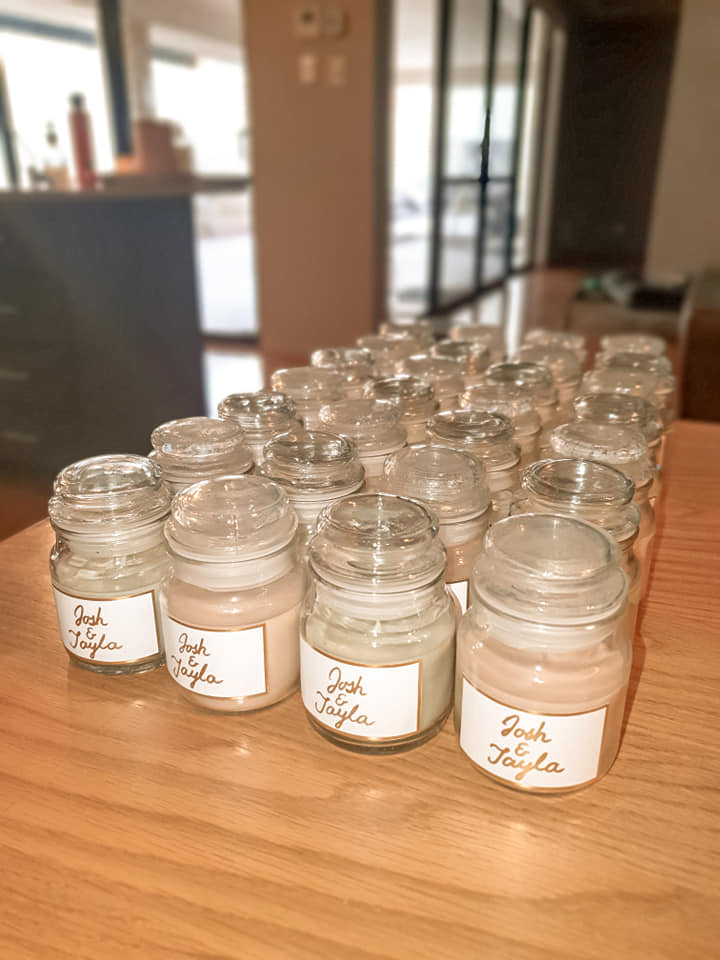 Four rows of candles in glass jars with labels that read 'Josh & Tayla' in gold pen