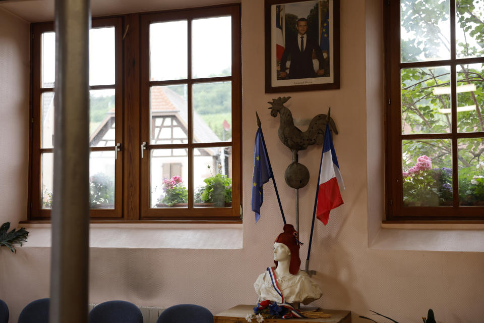 A portrait of French President Emmanuel Macron hangs above a statue of Marianne and a rooster, symbols of the French Republic and France, in a voting station in Soultz-Les-Bains, eastern France, Sunday, June 30, 2024. France is holding the first round of an early parliamentary election on Sunday that could bring the country's first far-right government since Nazi occupation during World War II. The second round is on July 7, and the outcome of the vote remains highly uncertain. (AP Photo/Jean-Francois Badias)