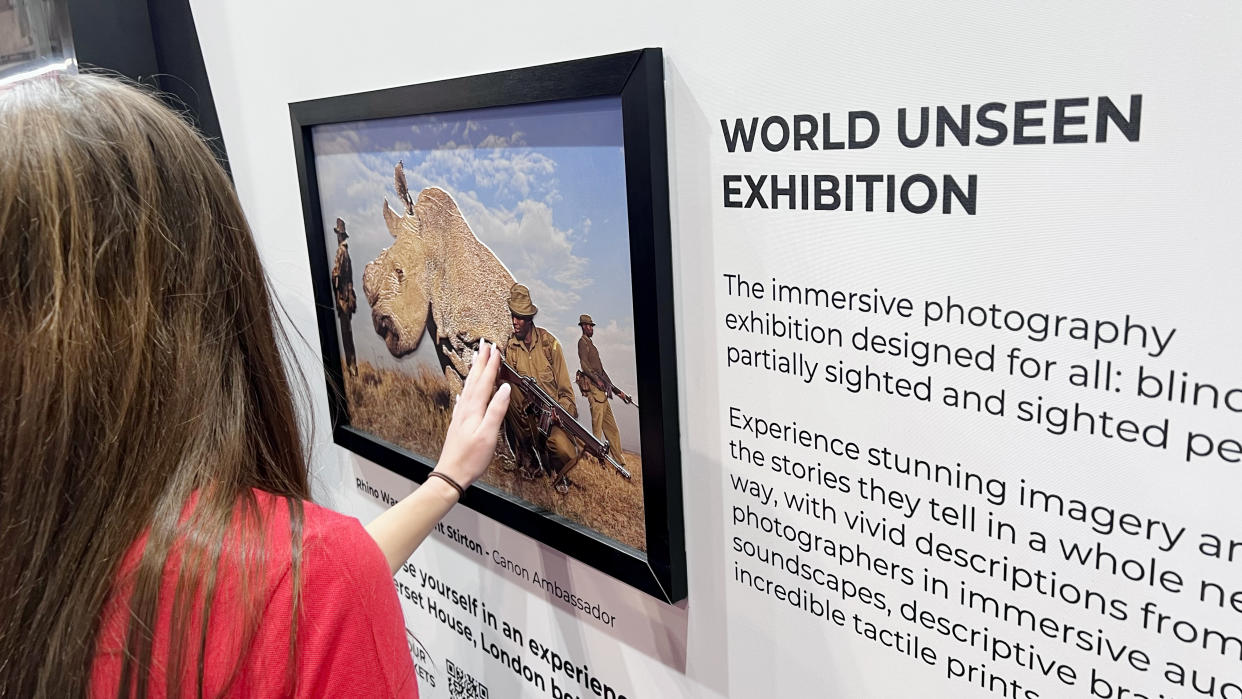  A lady in a red top feeling the tactile nature of an elevated photographic print of a rhino. 