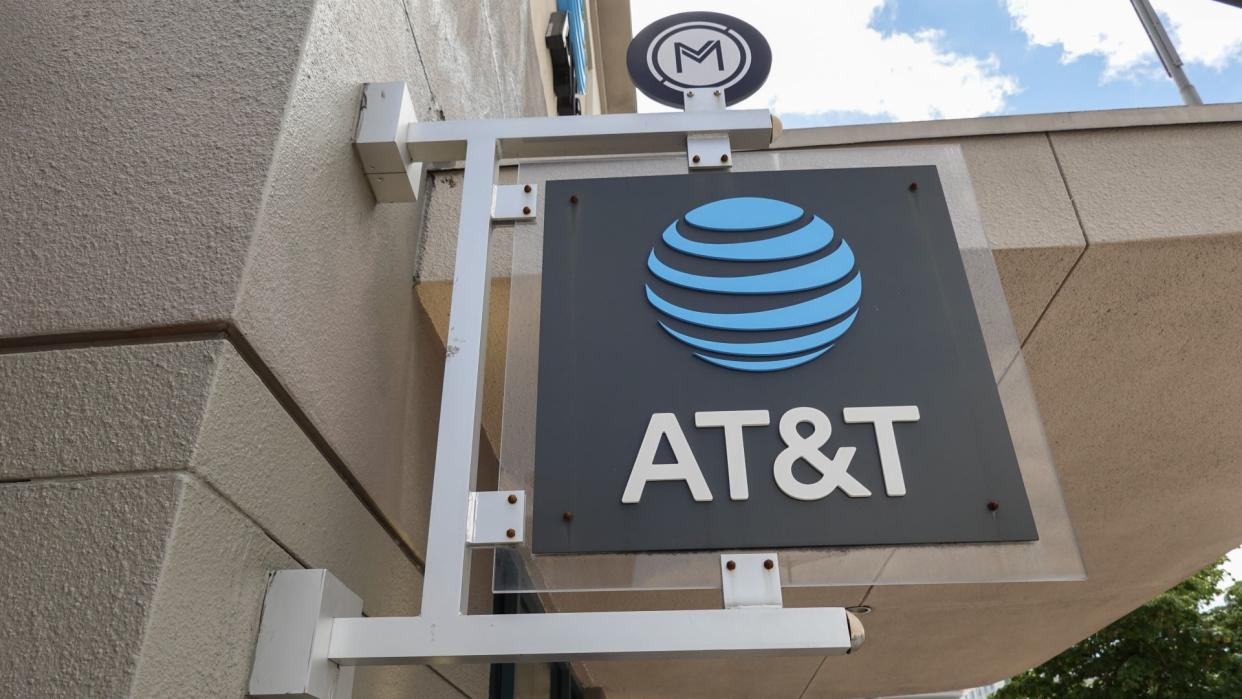  A black AT&T sign with its logo in bright blue hanging outside a brick store . 