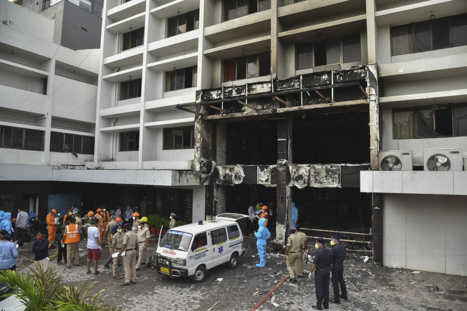 Rescuers and others stand outside Hotel Swarna Palace where a fire broke out early morning in Vijayawada, Andhra Pradesh state, India, Sunday, Aug. 9, 2020. The fire in the hotel being used as a COVID-19 facility killed seven coronavirus patients. (AP Photo)