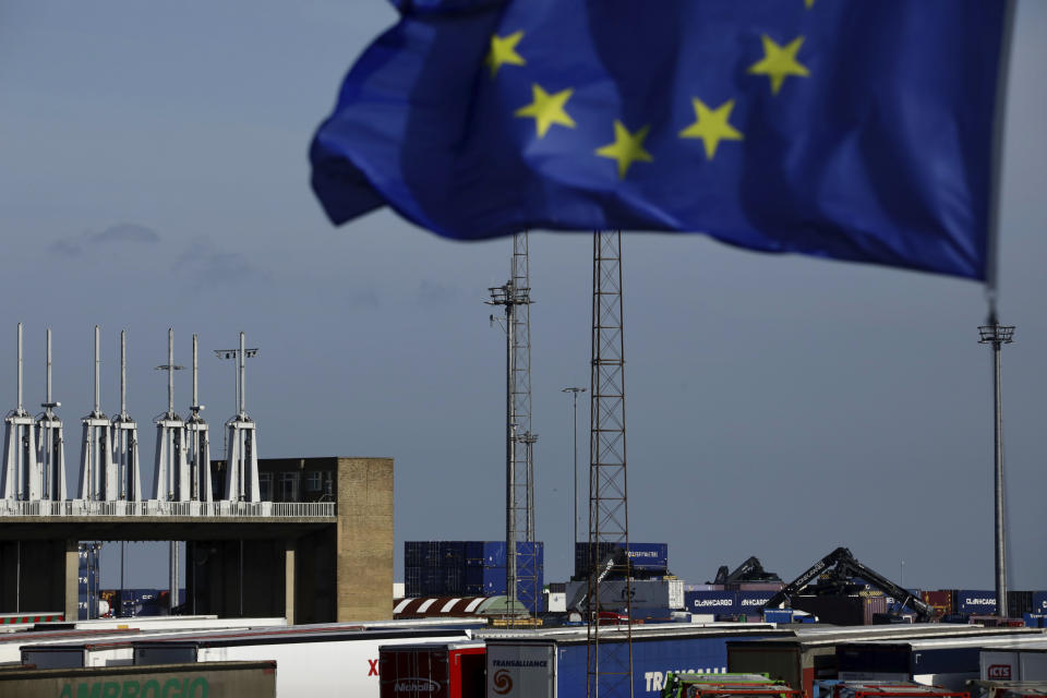 An EU flag flutters in the wind as workers lift containers to put onto trucks at the Port of Zeebrugge, in Zeebrugge, Belgium, Thursday, Oct. 24, 2019. British police raided two sites in Northern Ireland and questioned a truck driver as they investigated the deaths of 39 people found in a truck container at an industrial park in southeastern England. (AP Photo/Olivier Matthys)