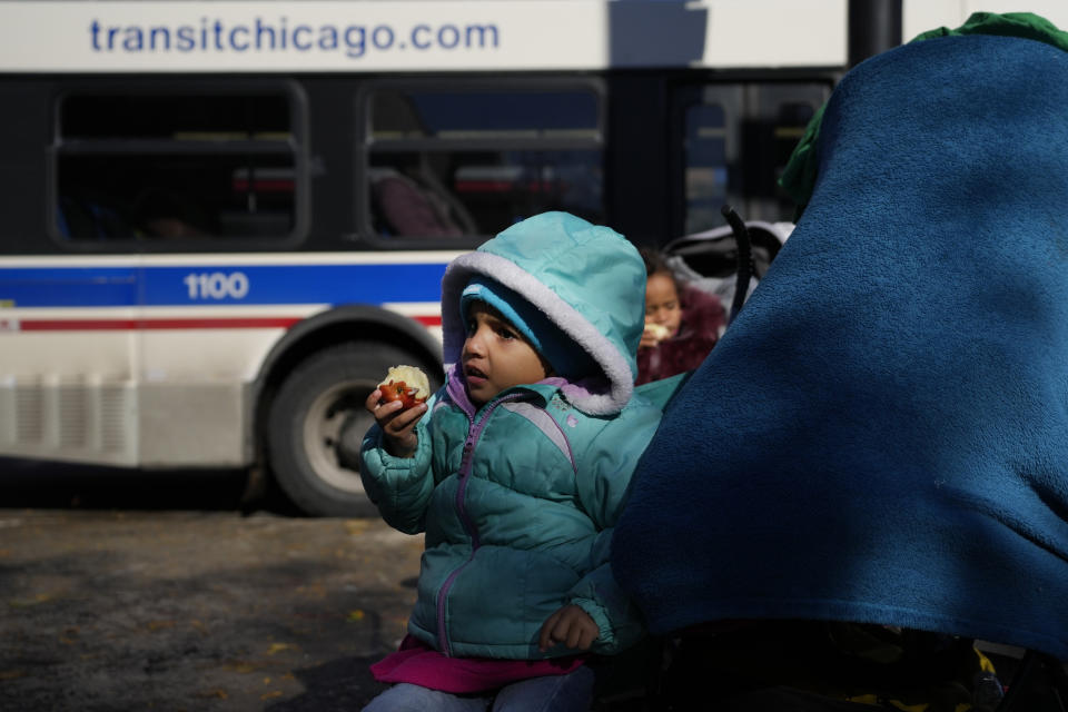 Two migrant girls eat apples next to a small migrant tent community, Wednesday, Nov. 1, 2023, near a Northside police station in Chicago. (AP Photo/Charles Rex Arbogast)