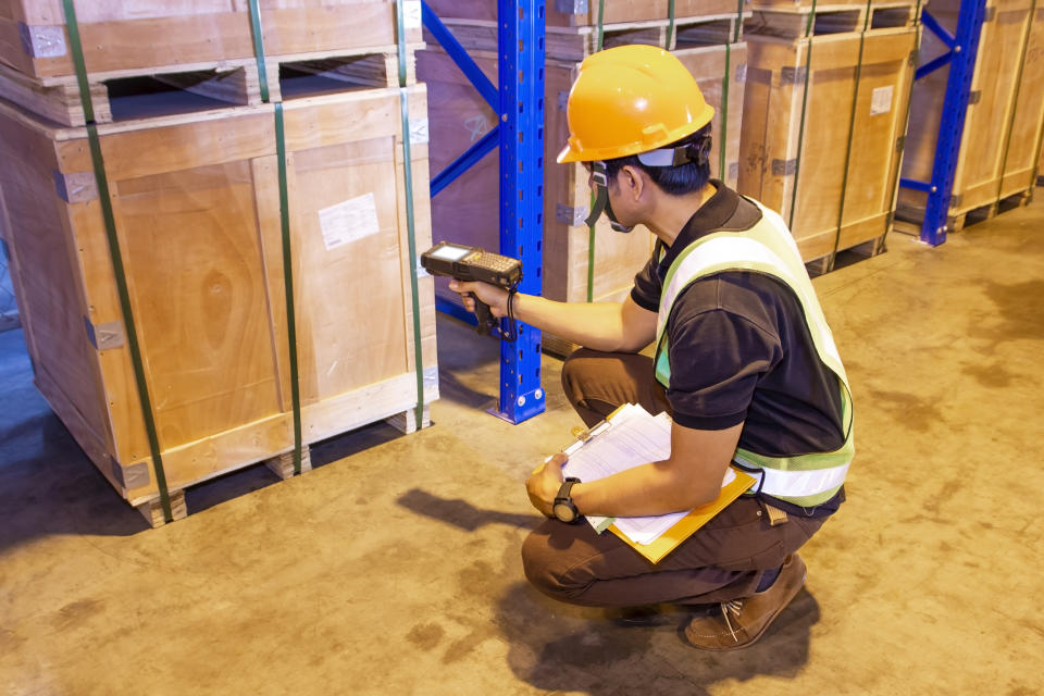 warehouse inventory management, worker in uniform hand holding bar code scanner with scanning on label of cargo pallet.