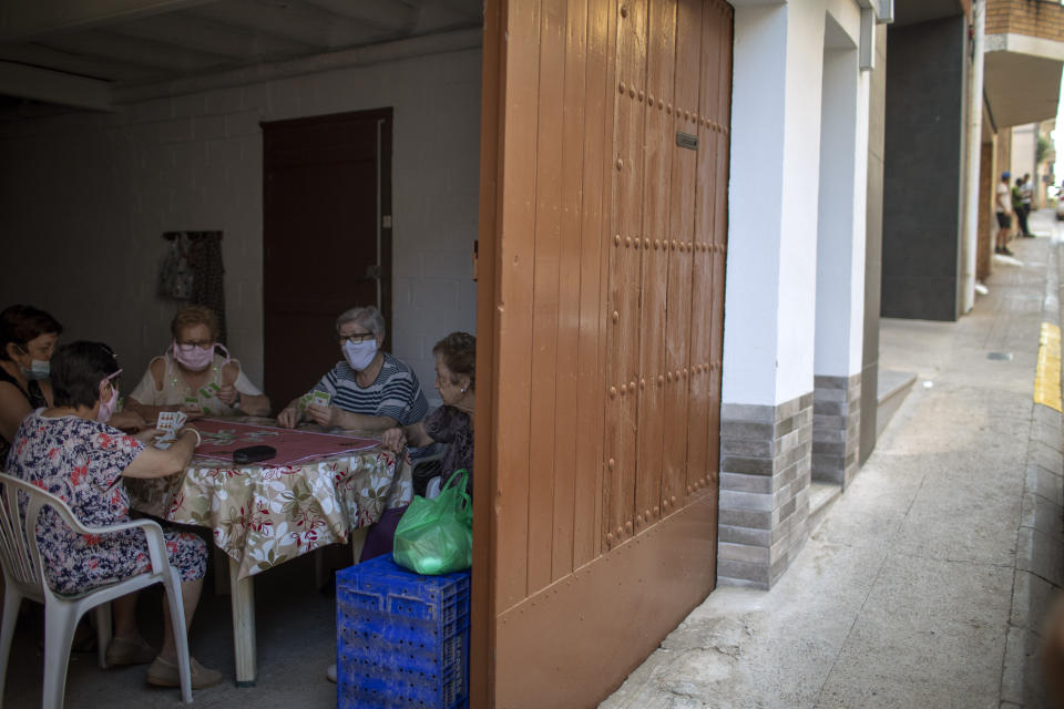 Women play cards inside a house as migrants seeking seasonal work harvesting fruit stand on the street in Fraga, Spain, Thursday, July 2, 2020. Authorities in northeast Spain have ordered the lockdown of a county around the city of Lleida due to worrying outbreaks of the COVID-19 virus. Catalan regional authorities announced Saturday, July 4, 2020 that as of noon local time movement will be restricted to and from the county of El Segriá around Lleida which is home to over 200,000 people. Residents will have until 4 p.m. to enter the area. The new outbreaks are linked to agricultural workers in the rural area. (AP Photo/Emilio Morenatti)