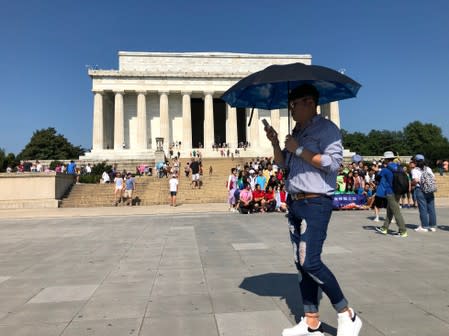 A tourist tries to shield himself from the sun using an umbrella in front of the Lincoln Memorial, on a day when the temperature was forecast to reach 99 degrees F, in Washington