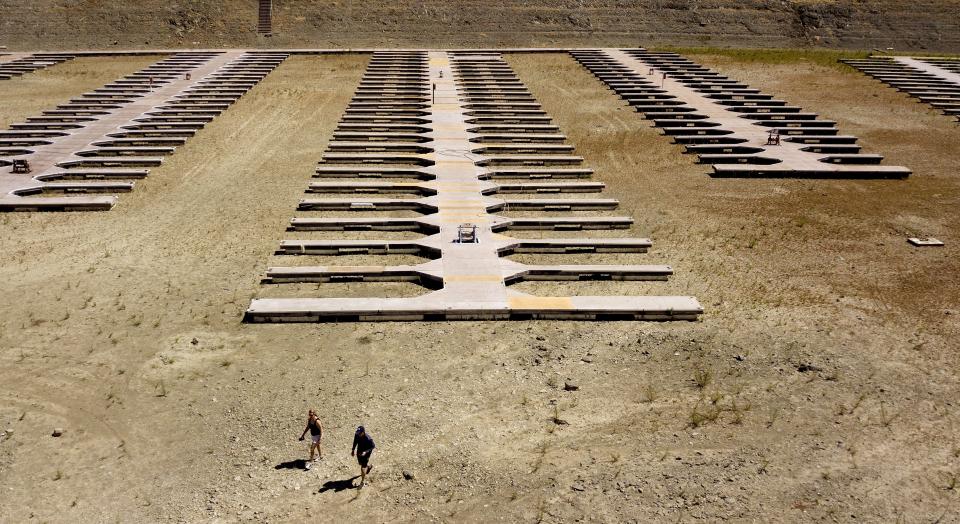 FILE - People walk near boat docks as they sit on dry land at the Browns Ravine Cove area of drought-stricken Folsom Lake in Folsom, Calif., on May 22, 2021. Months of winter storms have replenished California's key reservoirs after three years of punishing drought. (AP Photo/Josh Edelson, File)