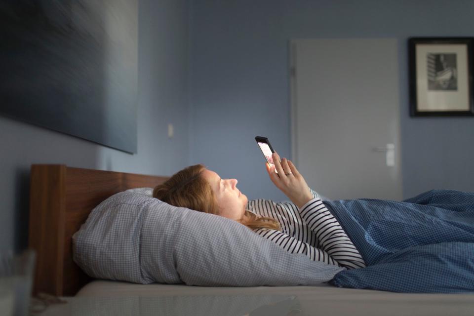 A young woman is lying in bed looking at her smartphone on February 13, 2018.