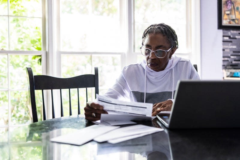 Woman paying bills using her laptop at her kitchen table - Photo: MoMo Productions (Getty Images)