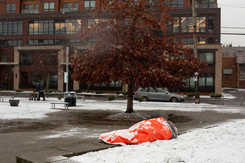 A homeless man, who said he was aware of the forecast for extreme weather, rests in a park while covered with snow on February 8, 2019 in Seattle, Washington. | David Ryder—Getty Images