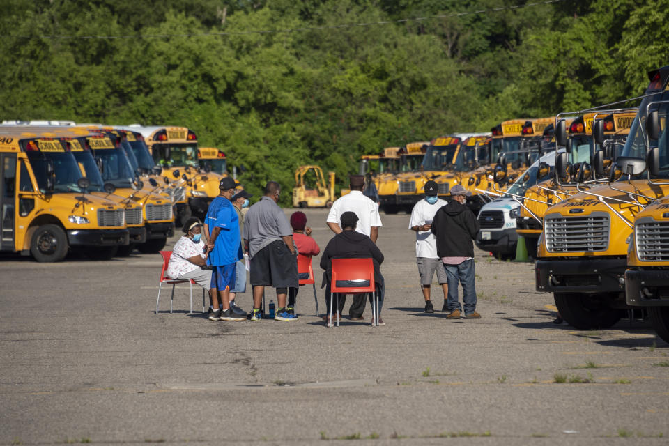 Workers sit around dozens of idle school buses after demonstrators blocked the driveways of the Detroit Public Schools West Side Bus Terminal to keep the buses from running on the first day of summer school, in Detroit, July 13, 2020. Concerns about COVID-19 and a lack of safety measures prompted the protesters to demand that schools close. (David Guralnick/Detroit News via AP) (David Guralnick/The Detroit News)/Detroit News via AP)