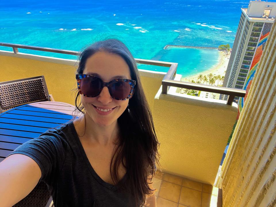 A woman standing on a balcony with views of the turquoise ocean.
