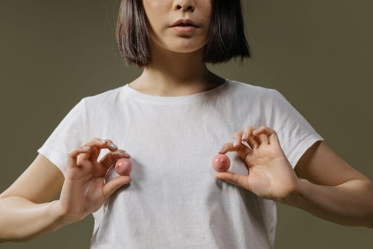 Woman in white plastic shirt holds up plastic nipples