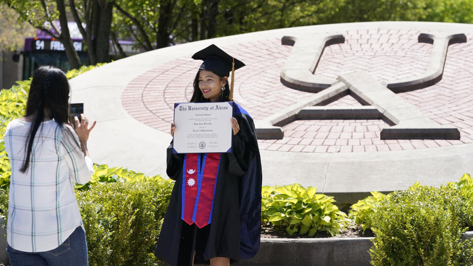 Recent University of Akron graduate Sulochana Shrestha, right, poses for a photo taken by her sister, Sushma, on campus, Thursday, May 13, 2021, in Akron, Ohio. Ohio Gov. Mike DeWine recently announced a weekly $1 million prize and full-ride college scholarships to entice more Ohioans to get the COVID-19 vaccine. (AP Photo/Tony Dejak)