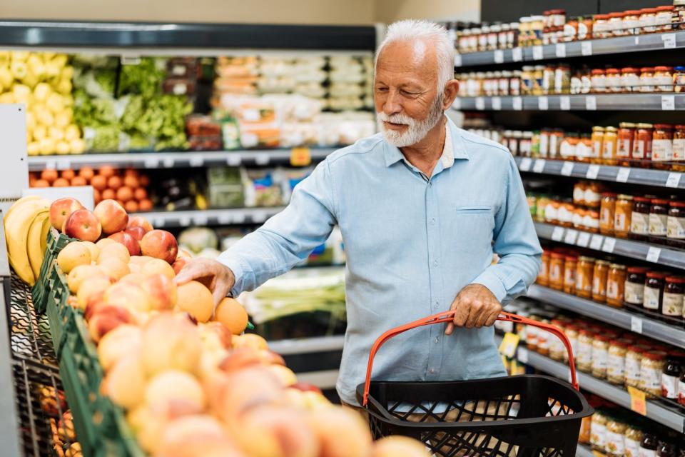 A person holding a basket and looking at produce in the grocery store.