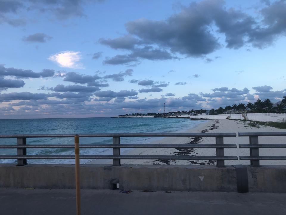 A view of the beach in Bimini as sun is starting to set over a cloudy sky and an empty stretch of sand.