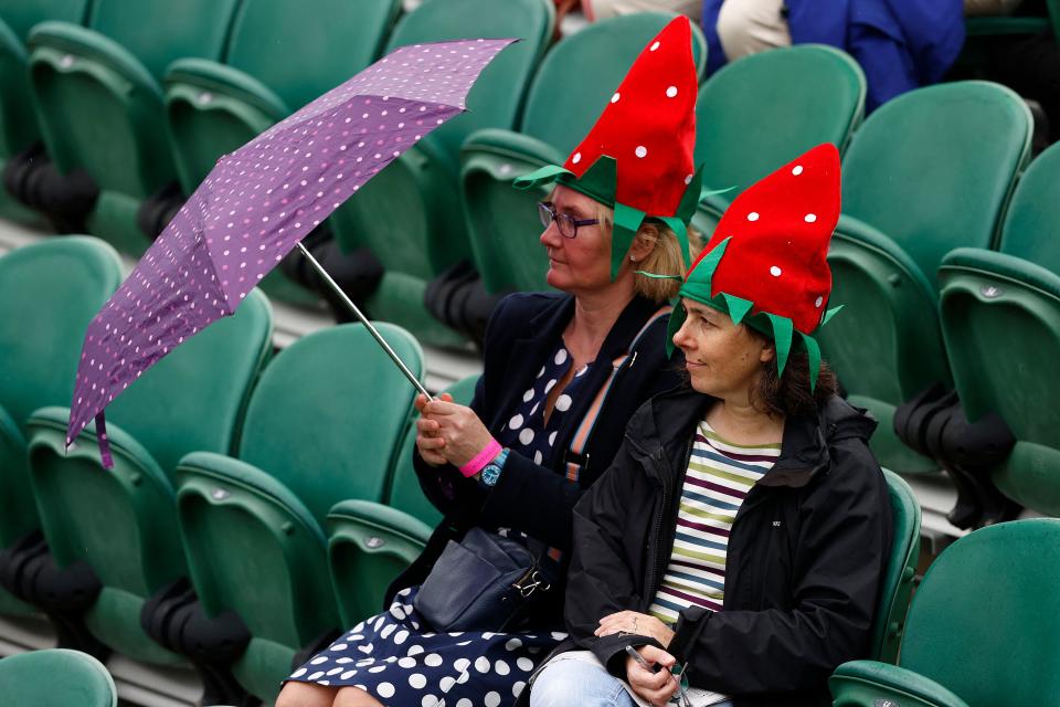 <p>Spectators wearing strawberry-themed hats shelter from the rain beneath an umbrella as they wait for play to begin on the first day of the 2021 Wimbledon Championships at the The All England Tennis Club in Wimbledon, southwest London, on June 28, 2021. - RESTRICTED TO EDITORIAL USE (Photo by Adrian DENNIS / AFP) / RESTRICTED TO EDITORIAL USE (Photo by ADRIAN DENNIS/AFP via Getty Images)</p>
