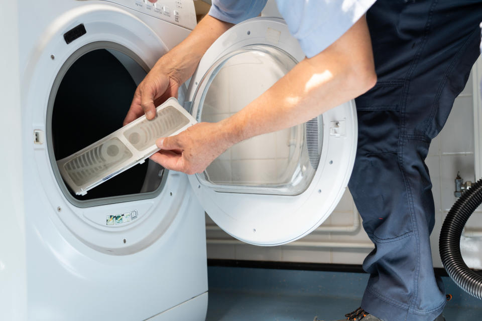 Hands holding a dryer lint basket above a clothes dryer