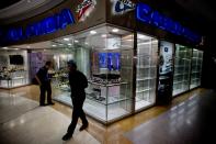 In this April 10, 2014 photo, customers walks past a Casio shop with half empty display cabinets at Sambil mall in Caracas, Venezuela. Since its inauguration in 1999, Caracas’ biggest mall has been a hive of frenzied shopping, a glitzy counterpoint to the anti-capitalist tirades of the late Hugo Chavez. Today, a few die-hard shoppers stroll through dimly lit corridors, past stained walls in need of a paint job, and shuttered boutiques. In those stores that are open, employees try to spread out their dwindling supply of garments, cellphones and designer bags on shelves and window displays, a futile attempt to mask scarce inventory. (AP Photo/Fernando Llano)