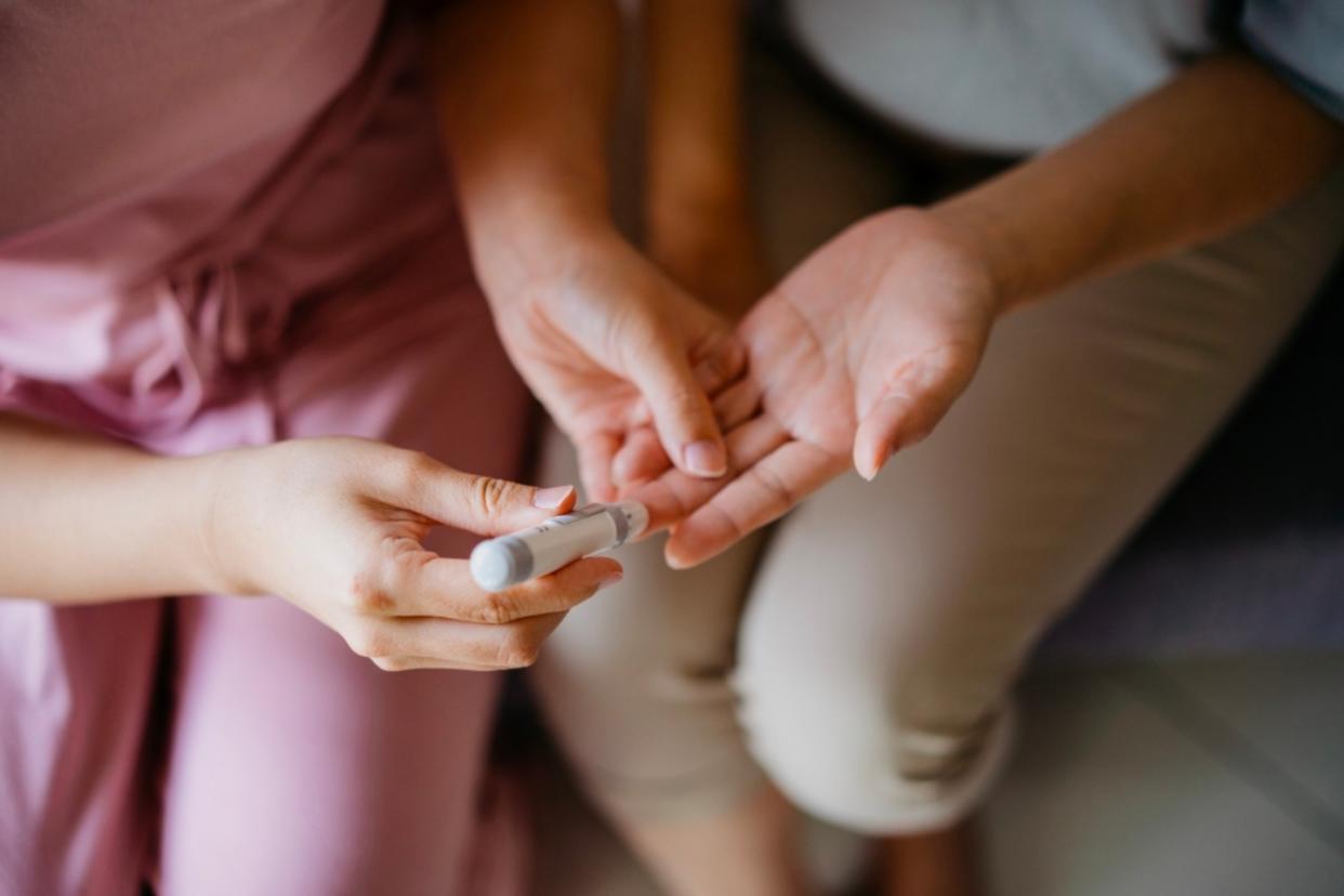 A woman draws blood from a patient's middle finger using a lancet to run low blood sugar test.