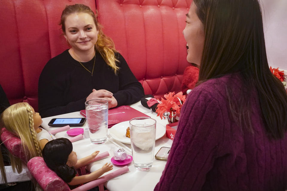 Marisa Dragos, 23, left, along with her childhood friend Lisa Costantino, 24, right, sit for lunch at American Girl Cafe with two store-borrowed dolls, Friday, Dec. 2, 2022, in New York. "I still have the dolls, just kind of sitting in my room," said Dragos about her American Dolls at home. "They are my little friends that I hang out with." (AP Photo/Bebeto Matthews)