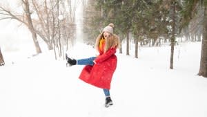 Side view of delighted female in warm clothes jumping and playing with snow in winter garden in city and looking at camera