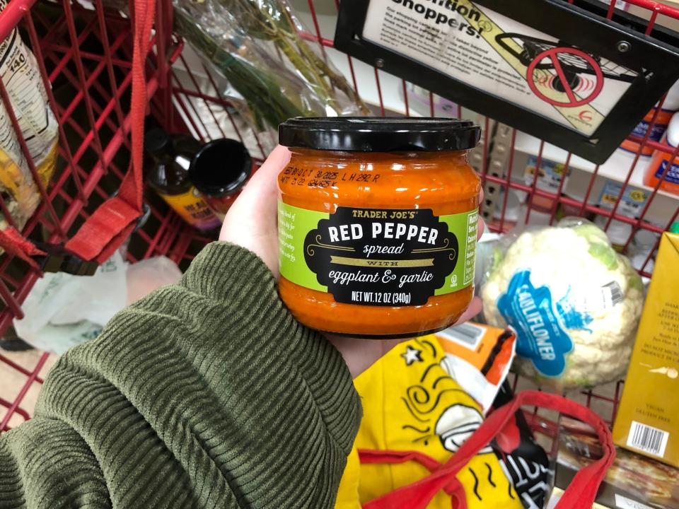 A hand holding a jar of Trader Joe's red-pepper spread with eggplant and garlic.