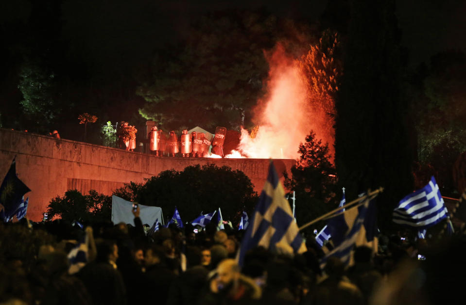 A flare thrown by opponents of Prespa Agreement, attending a rally outside the Greek Parliament, burns in front of police officers in riot gear guarding one of its entrances in Athens, Thursday, Jan. 24, 2019. Greek lawmakers are debating a historic agreement aimed at normalising relations with Macedonia in a stormy parliamentary session scheduled to culminate in a Friday vote. (AP Photo/Thanassis Stavrakis)