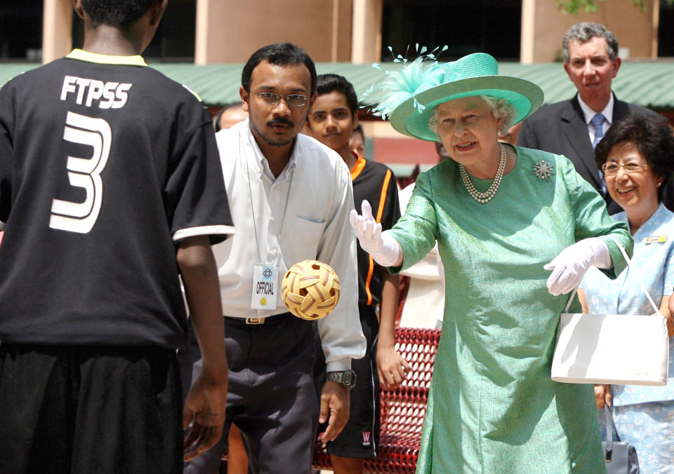 Queen Elizabeth II serves a sepak takraw player with a rattan ball during her tour around Toa Payoh on 17 March 2006. 