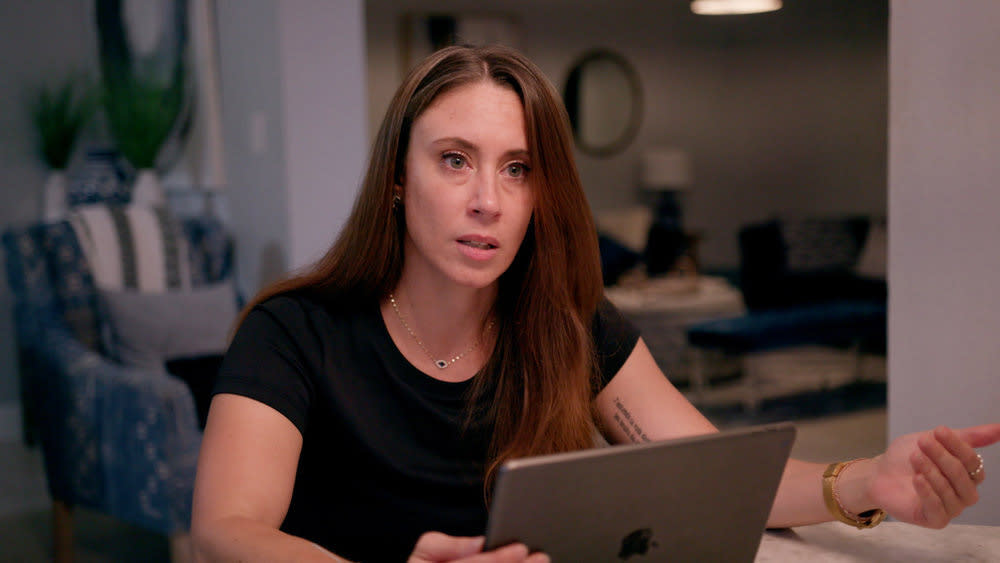 Casey Anthony in a black t-shirt looks slightly off camera in front of an ipad. she's gesturing with her left hand, palm upwards. (Peacock / NBC Universal)