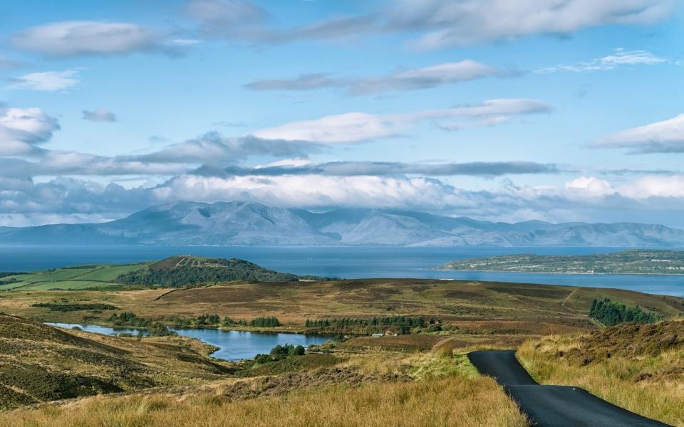 Hills, touched by clouds in distance, with water and rolling green in front of it  - jimmcdowall /iStockphoto 