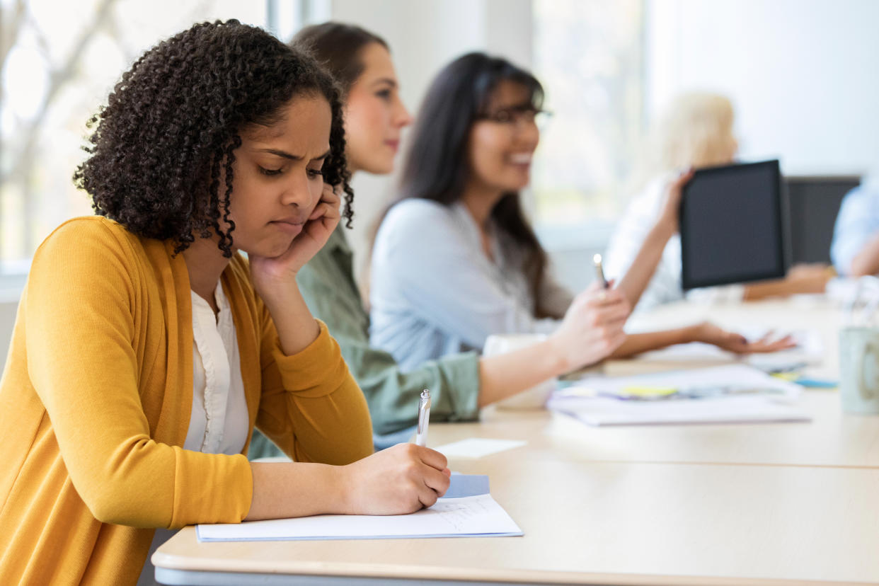 A young adult design professional sitting at a desk frowns as she brainstorms project ideas.