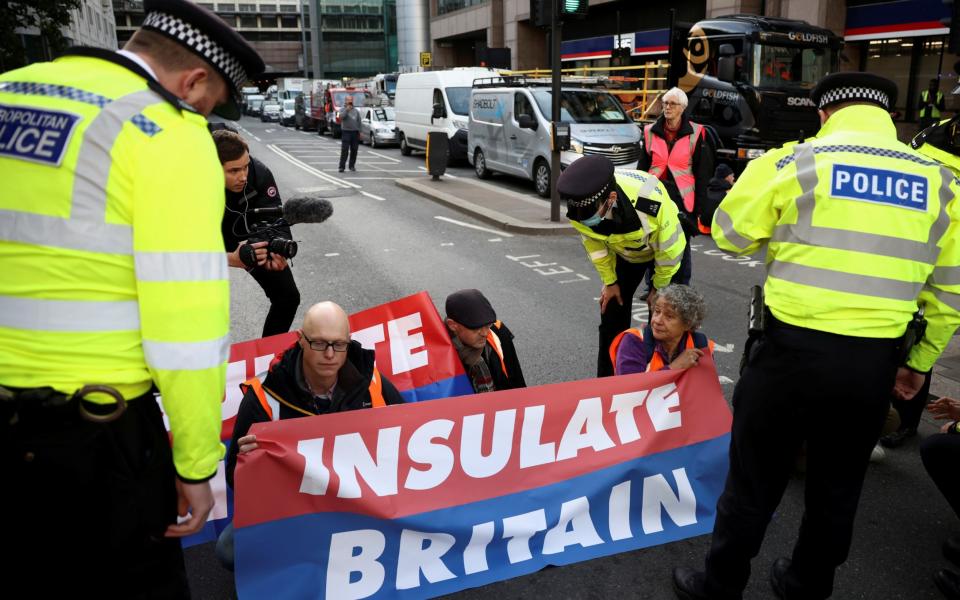 Insulate Britain protesters block a road next to police officers in London on 25 October 2021. Some protesters glued their heads and hands to roads to lengthen the time it takes to remove them. - Henry Nicholls/Reuters