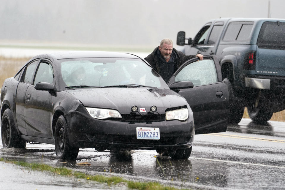 A motorist pushes his car off the roadway after the engine stopped while driving through water over the roadway on Highway 20, Monday, Nov. 15, 2021, near Hamilton, Wash. The heavy rainfall of recent days brought major flooding of the Skagit River that is expected to continue into at least Monday evening. (AP Photo/Elaine Thompson)