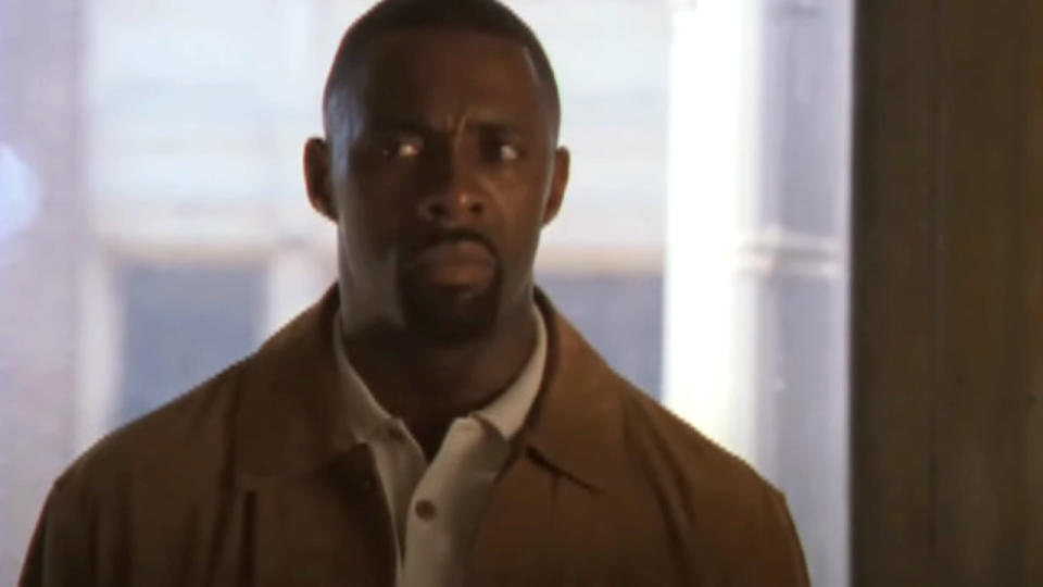 Idris Elba stands in front of a window with a look of concern in The Wire.