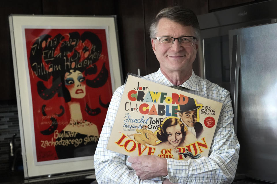 Dwight Cleveland, a major collector of movie posters and lobby cards, poses for a portrait with a lobby card and movie poster Tuesday, Sept. 27, 2022, in Chicago. Many silent films from the early 1900s no longer exist. But they live on in movie theater lobby cards. More than 10,000 of the mostly 11-by-14-inch cards that promoted the cinematic romances, comedies and adventures of the era are being digitized for preservation and publication online, thanks to an agreement formed between a Chicago-based collector Cleveland and Dartmouth College. (AP Photo/Charles Rex Arbogast)