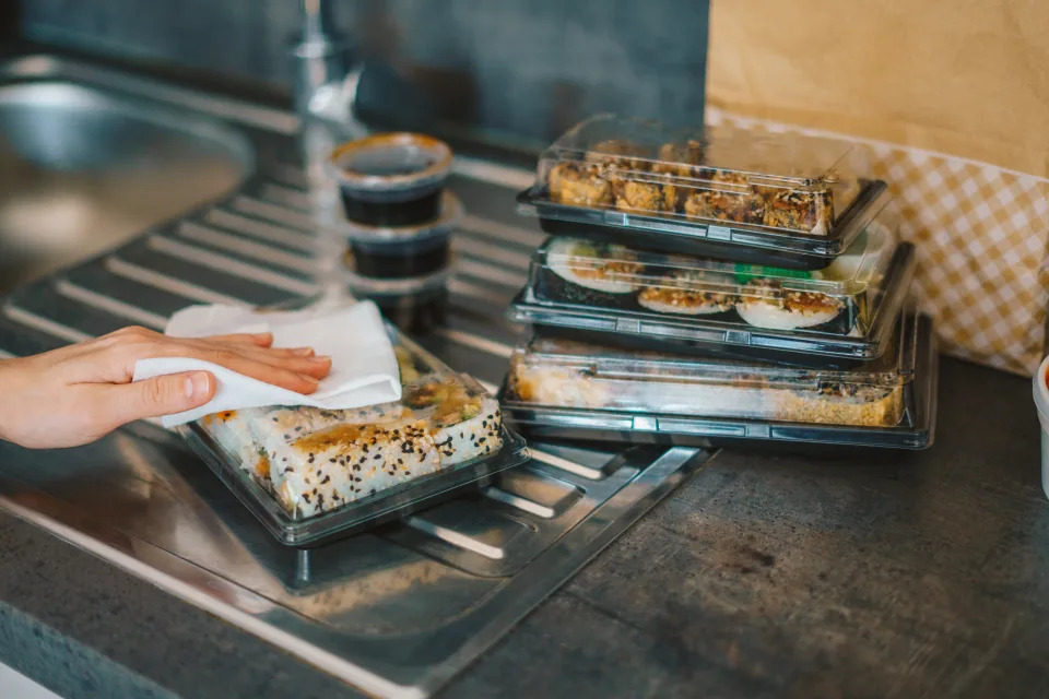 Woman disinfecting takeaway sushi boxes with a wet wipe at home