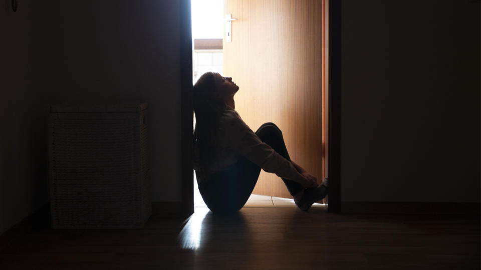 Backlit photo of a teenager sitting in an indoor doorway.