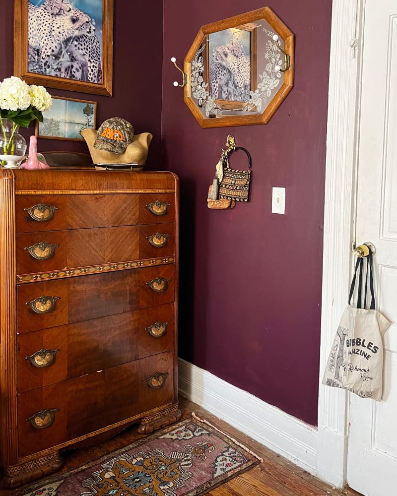 Wood dresser in corner of eggplant bedroom.