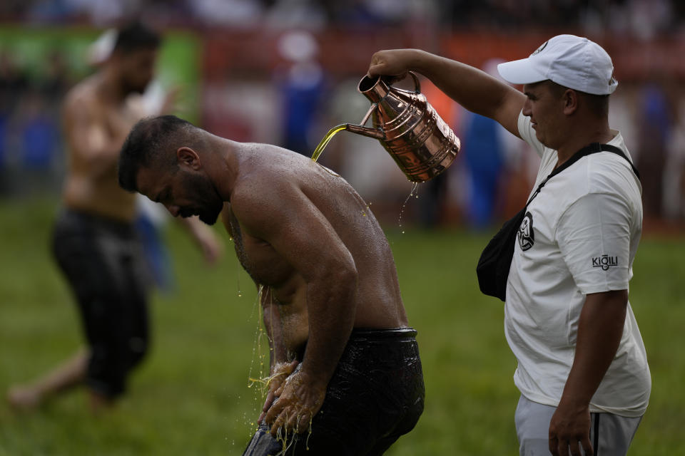 A wrestler is doused in oil by an 'oiler, during the 663rd annual Historic Kirkpinar Oil Wrestling championship, in Edirne, northwestern Turkey, Saturday, July 6, 2024. Wrestlers take part in this "sudden death"-style traditional competition wearing only a pair of leather trousers and a good slick of olive oil. The festival is part of UNESCO's List of Intangible Cultural Heritages. (AP Photo/Khalil Hamra)