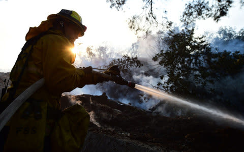 A firefighter controls flames burning in a home at the Skirball Fire in the upscale Bel- Air section of west Los Angeles - Credit: AFP