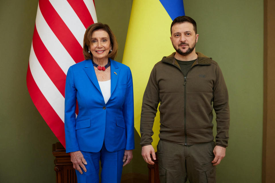 Pelosi and Zelensky stand side by side in front of flags.