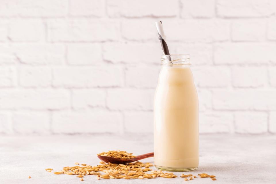 A bottle of oat milk and oats on a light background.