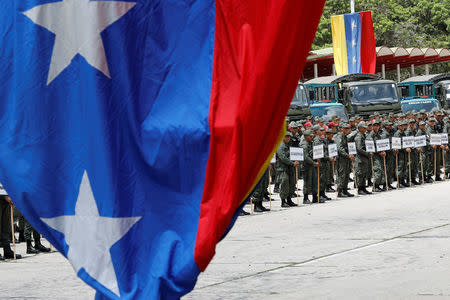 Venezuela's flag is seen next to soldiers standing in formation before the start of a ceremony to kick off the distribution of security forcers and voting materials to be used in the upcoming presidential elections, at Fort Tiuna military base in Caracas, Venezuela May 15, 2018. REUTERS/Carlos Jasso