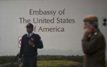 A U.S. embassy security guard (L) and an Indian policeman stand in front of the main gate of the embassy as the bulldozer (unseen) removes the security barriers, in New Delhi December 17, 2013. Indian authorities removed security barriers in front of the U.S. embassy in New Delhi on Tuesday apparently in retaliation for the arrest and alleged heavy-handed treatment of an Indian diplomat in New York. New Delhi police used tow trucks and bulldozers to remove the concrete barricades, which are used to restrict traffic on the road outside the embassy. REUTERS/Adnan Abidi (INDIA - Tags: POLITICS)